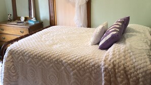 Een slaapkamer met een bed, nachtkastje, spiegel en een foto aan de muur.