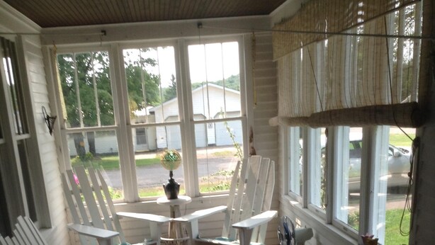 Een overdekt terras met witte meubels, waaronder stoelen en een tafel, en een kleine potplant.