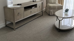 Une chambre d’hôtel dotée d’un téléviseur à écran plat fixé au mur, d’une console en bois avec des tiroirs, d’un fauteuil à motifs et d’une petite table ronde sur laquelle est posé un objet décoratif.