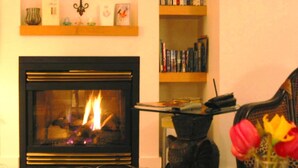 A living room with a fireplace, a bookshelf, and a decorative vase with flowers. - WATER'S EDGE DOWNTOWN SUNSET WEST BALC, KING BDRM, A/C, 90 DAY MIN, (Victoria)
