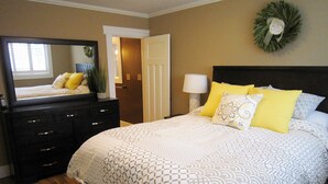 Un dormitorio con cama, cómoda, espejo y una puerta que da a otra habitación.