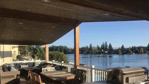 Una terraza cubierta al aire libre con vista a un lago, muebles de madera y una parrilla de barbacoa.