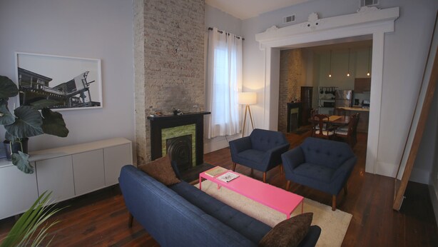 A living room with a fireplace, blue sofas, a pink coffee table, and a dining area visible through an open doorway. - Elegant home steps from St. Charles Ave, parades, and downtown attractions. (New Orleans)