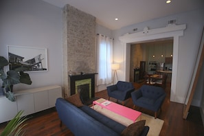Una sala de estar con chimenea, sofás azules, una mesa de centro rosa y un comedor visible a través de un arco.