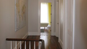 A hallway with a wooden staircase, a map on the wall, and a door leading to a room with yellow walls. - Elegant home steps from St. Charles Ave, parades, and downtown attractions. (New Orleans)