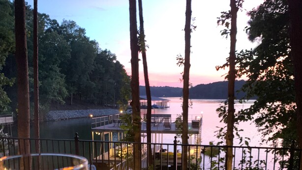 Un foyer extérieur, une bouteille de vin à portée de main, avec vue sur un lac, une terrasse en bois et une rambarde.