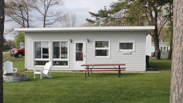 Een klein, laag gebouw met een terras, een vuurkuil en twee witte Adirondack stoelen.