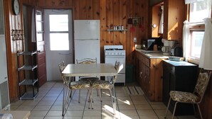 Een kleine keuken met een koelkast, fornuis en eettafel met stoelen.