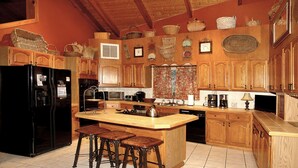 A kitchen with wooden cabinets, a black refrigerator, a stove, and a sink. There are three stools at the island. - Private, Secluded, Quiet with Large Creek sitting on over 6 acres of wooded land (Gatlinburg)