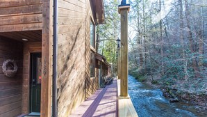 A wooden cabin with a deck overlooking a river, surrounded by forest. - Private, Secluded, Quiet with Large Creek sitting on over 6 acres of wooded land (Gatlinburg)
