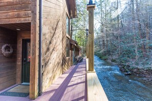 Eine Holzhütte mit einer Terrasse, die auf einen Fluss mit Blick auf einen Wald blickt.