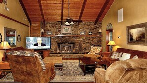 A cozy living room with a stone fireplace, wooden beams, and a television displaying a show. - Private, Secluded, Quiet with Large Creek sitting on over 6 acres of wooded land (Gatlinburg)