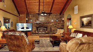 Ein gemütliches Wohnzimmer mit Kamin aus Stein, Holzbalken und einem Fernseher, der eine Fernsehsendung zeigt.