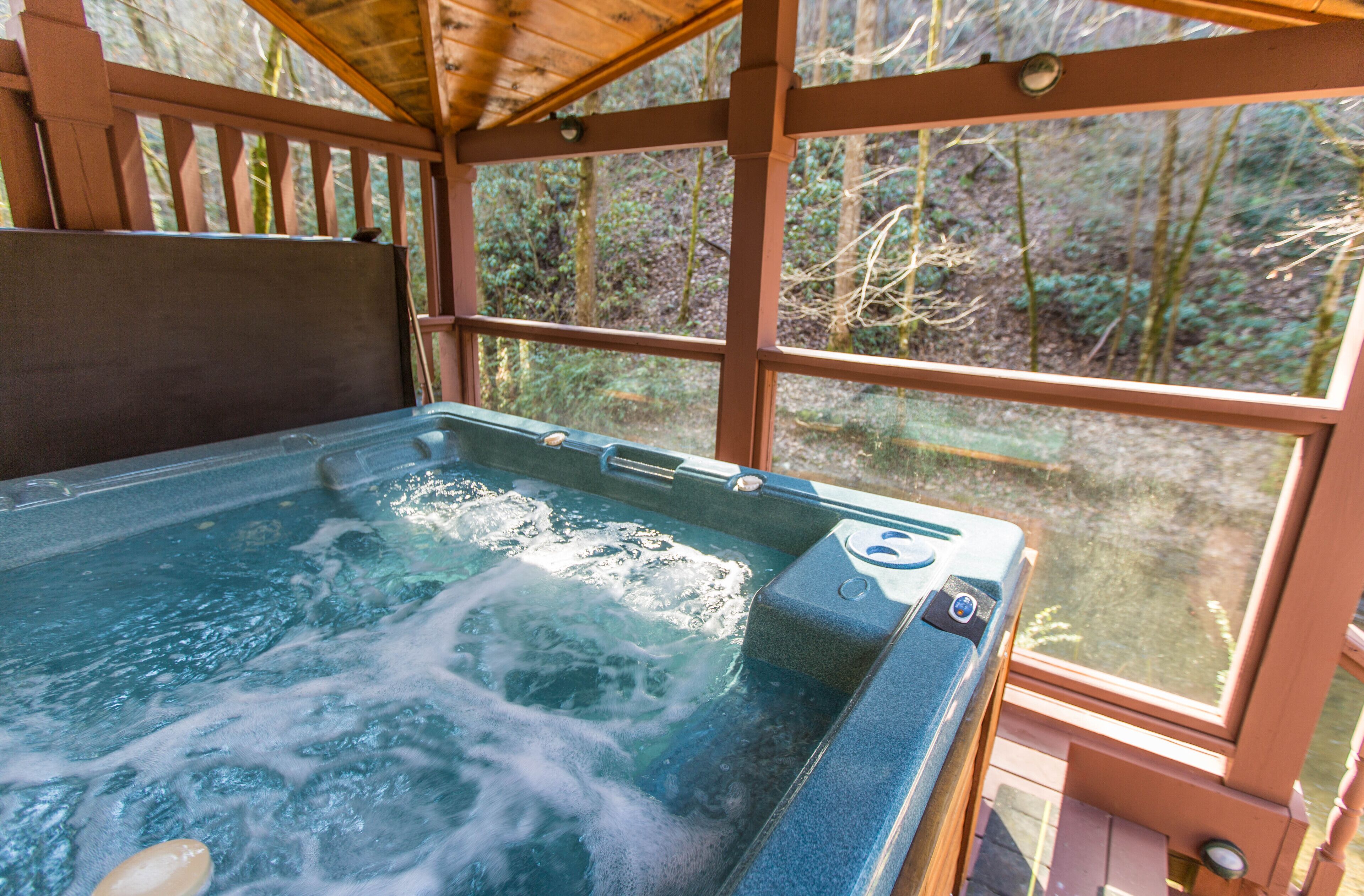 A hot tub with a wooden deck and large windows overlooking a forest.
