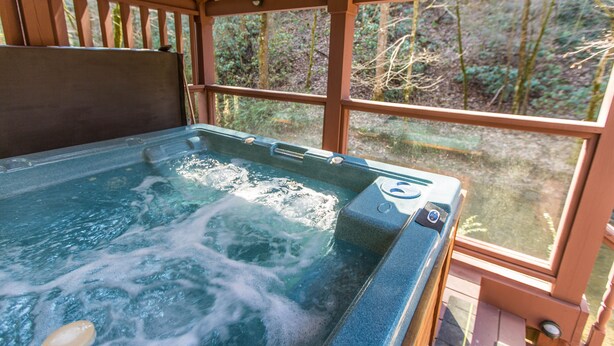 A hot tub with a wooden deck and large windows overlooking a forest. - Private, Secluded, Quiet with Large Creek sitting on over 6 acres of wooded land (Gatlinburg)