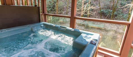 Un bain à remous doté d’une terrasse en bois et de grandes fenêtres donnant sur une forêt.