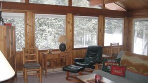 A cozy cabin interior with wooden walls, large windows, a leather chair, a sofa, and a small table. - Mt Bachelor, Deschutes River Cozy Cabin w/HotTub, Minutes to Sunriver (Bend)