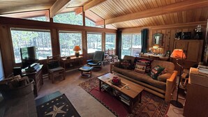A spacious living room with a large window, wooden ceiling, and a cozy seating area with a sofa and chairs. - Mt Bachelor, Deschutes River Cozy Cabin w/HotTub, Minutes to Sunriver (Bend)