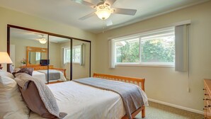 Une chambre à coucher avec un lit, un ventilateur de plafond, un grand miroir et une fenêtre avec des rideaux.
