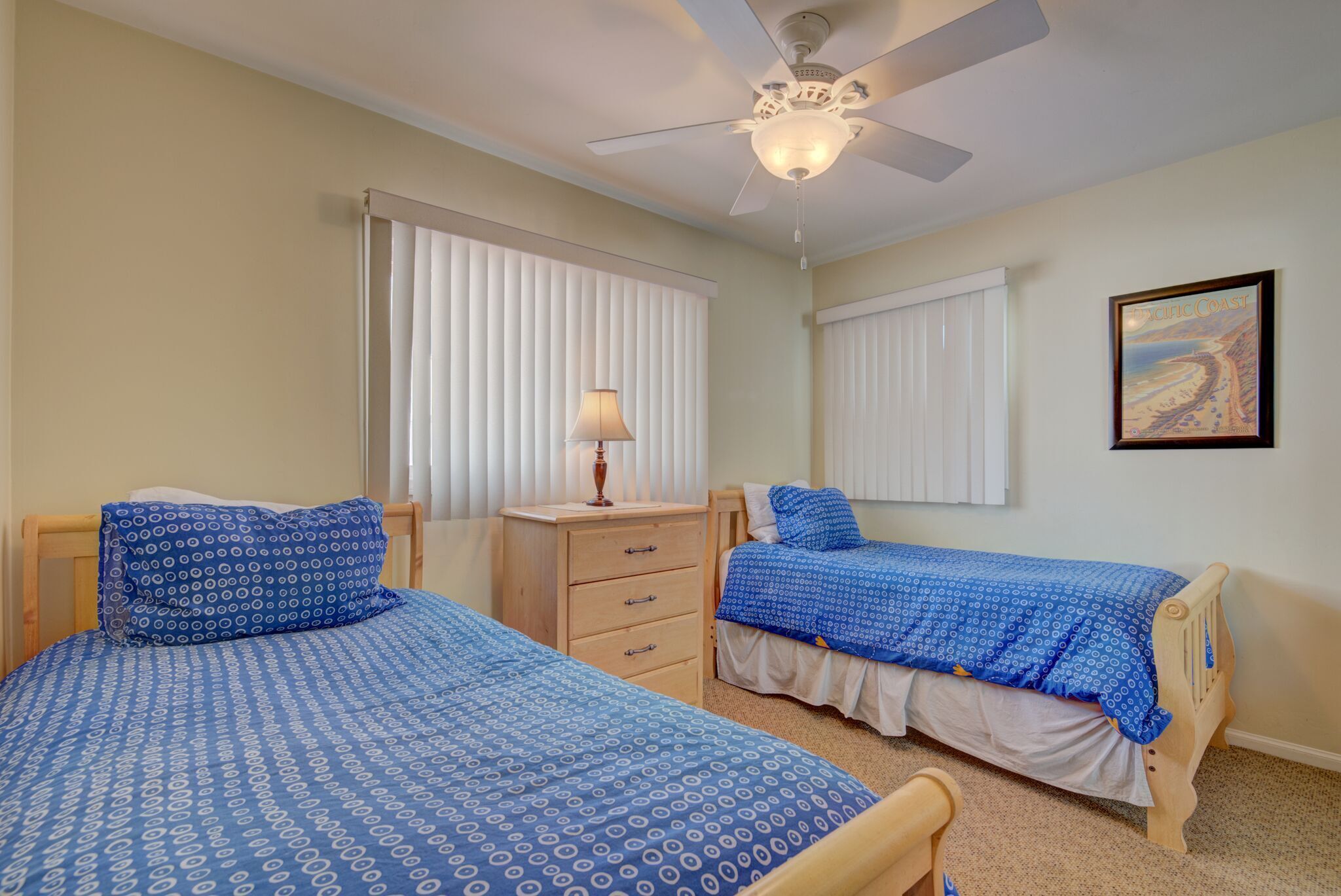 A bedroom with two beds, a ceiling fan, and a lamp.