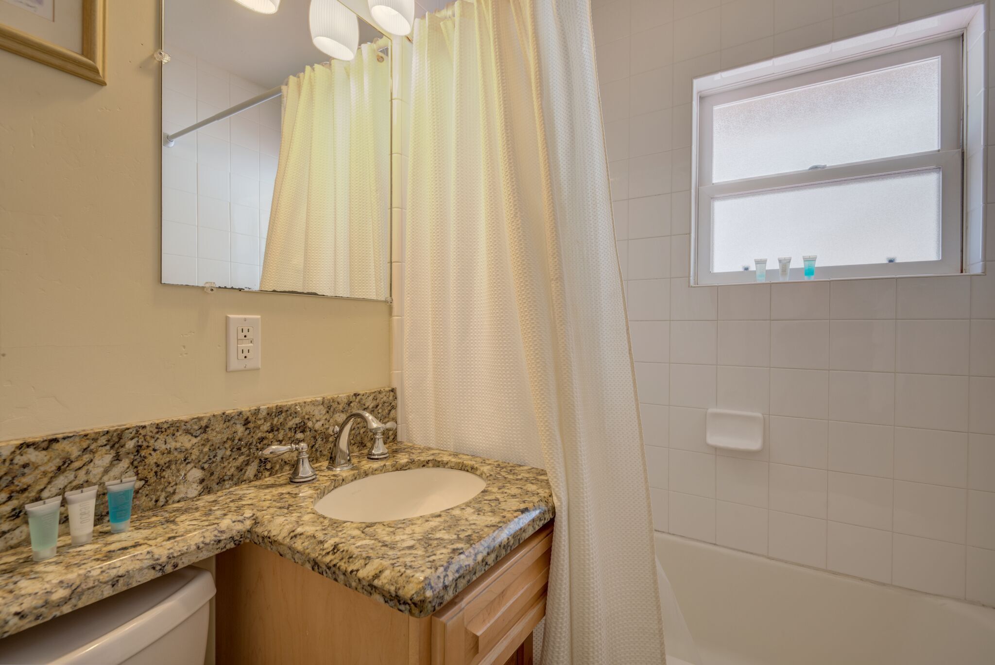 A bathroom with a granite countertop sink, a mirror, a window with a view, and a shower curtain.