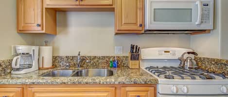 A kitchen with wooden cabinets, a granite countertop, a microwave, a stove, and a coffee maker.
