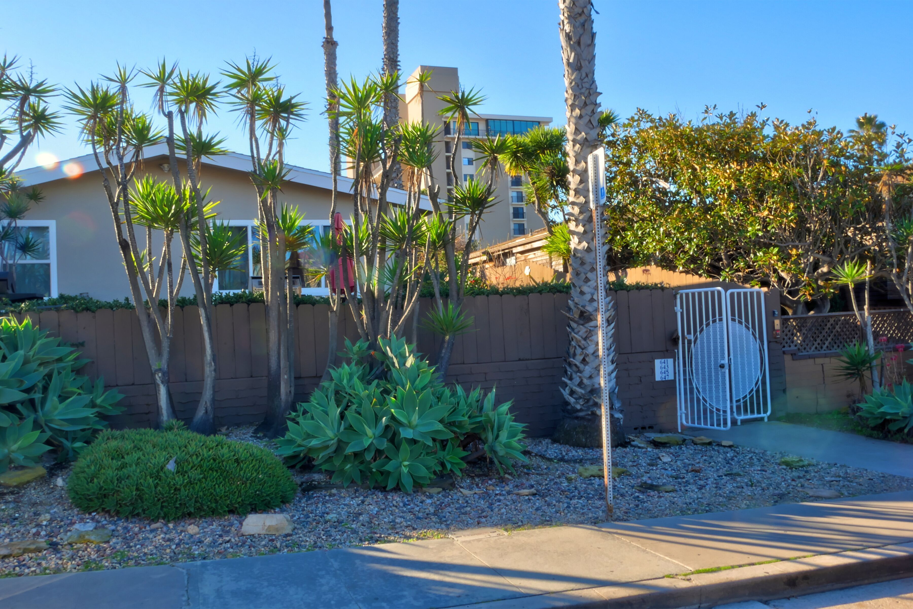 A gated residential area with palm trees, a building with a beige facade, and a white gate.