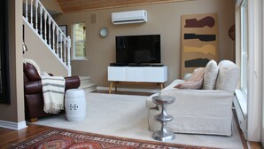 Un salon avec un escalier, un téléviseur à écran plat, un canapé blanc et un tapis à motifs.