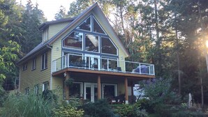 Une maison à deux étages dotée d’un balcon, entourée d’une végétation luxuriante.