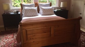 Un lit en bois avec quatre oreillers, dans une pièce dotée d’une grande fenêtre, d’une table de chevet et d’une lampe.