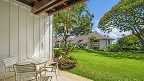Une terrasse avec une table et des chaises, un mur extérieur blanc et une vue sur une pelouse bien entretenue et des maisons au loin.