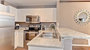 A modern kitchen with white cabinets, stainless steel appliances, a granite countertop, and a decorative mirror on the wall.