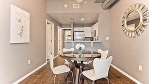 A dining area with a round glass table, white chairs, and a vase with flowers.