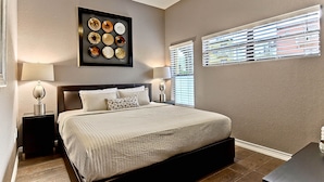 A bedroom with a large bed, two bedside tables, a wall-mounted light fixture, and a window with blinds.