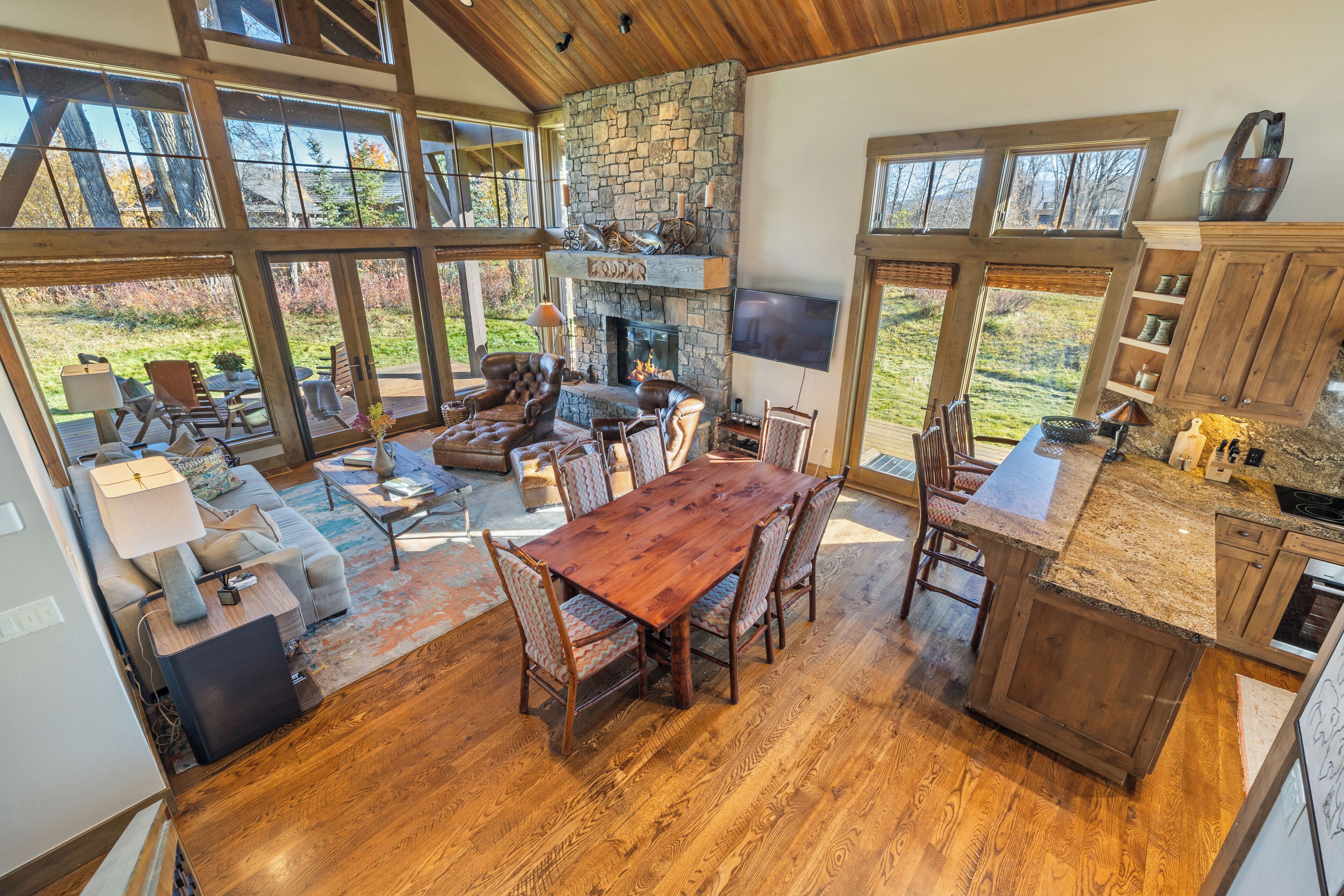 A spacious living area with a stone fireplace, large windows, and a wooden dining table.