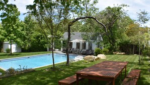 A backyard with a swimming pool, wooden patio furniture, and a house in the background.