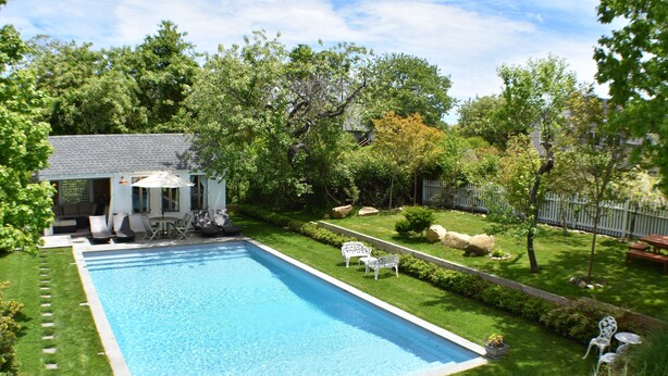 A rectangular swimming pool with a small deck area, surrounded by a well-maintained lawn and trees.