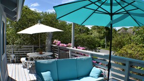 A deck with a blue sofa, a white table, and a turquoise umbrella.