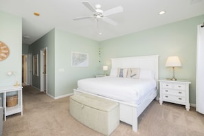 A bedroom with a bed, nightstands, a lamp, a ceiling fan, a map on the wall, and a door leading to another room. - Stay at Sail Away - Riverfront Views (Folly Beach)