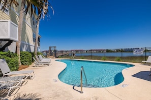 A swimming pool with lounge chairs, a lifeguard tower, and a view of a body of water.