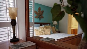 Un dormitorio con una cama, una mesita de noche con libros, una lámpara y un espejo grande que refleja la habitación.