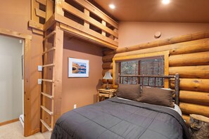 A log cabin bedroom with a bed, a ladder, a nightstand, a lamp, and a framed picture on the wall.