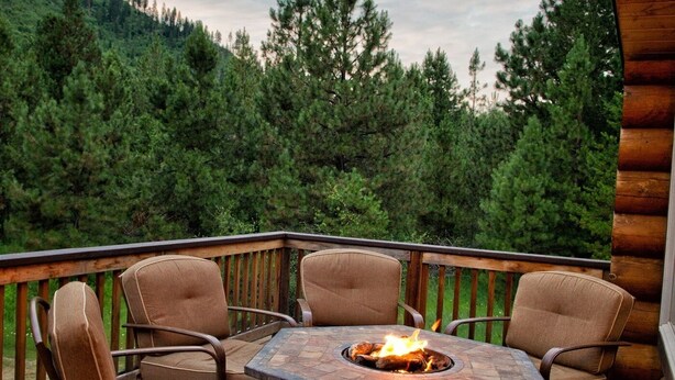 A wooden deck with a stone fire pit table and four chairs.