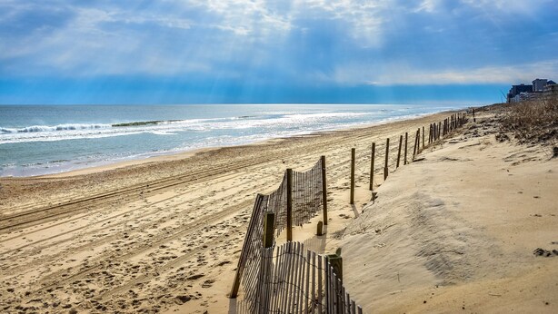 A beach with a wooden fence and buildings in the background. - Charming 3BR 2BA Unit, Close to the Beach, Great Restaurants and Shopping! (Ocean City)