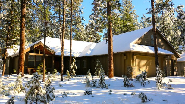 Lumihunnun peittämä hirsimökki, jonka ympärillä kohoaa korkeita mäntyjä.