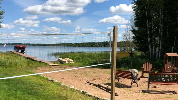 Zona de pícnic al costat del llac, amb una banca de fusta, una petita construcció de fusta i un vehicle vermell estacionat a la vora de l'aigua.