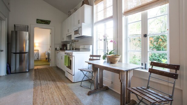 A kitchen with a wooden table, chairs, a refrigerator, and a window with a view of greenery. - Historic Uptown Cottage - 1 mile to Tulane & Loyola (New Orleans)