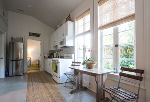Una cocina con una mesa de madera, sillas, un refrigerador y una ventana con vista a la vegetación.