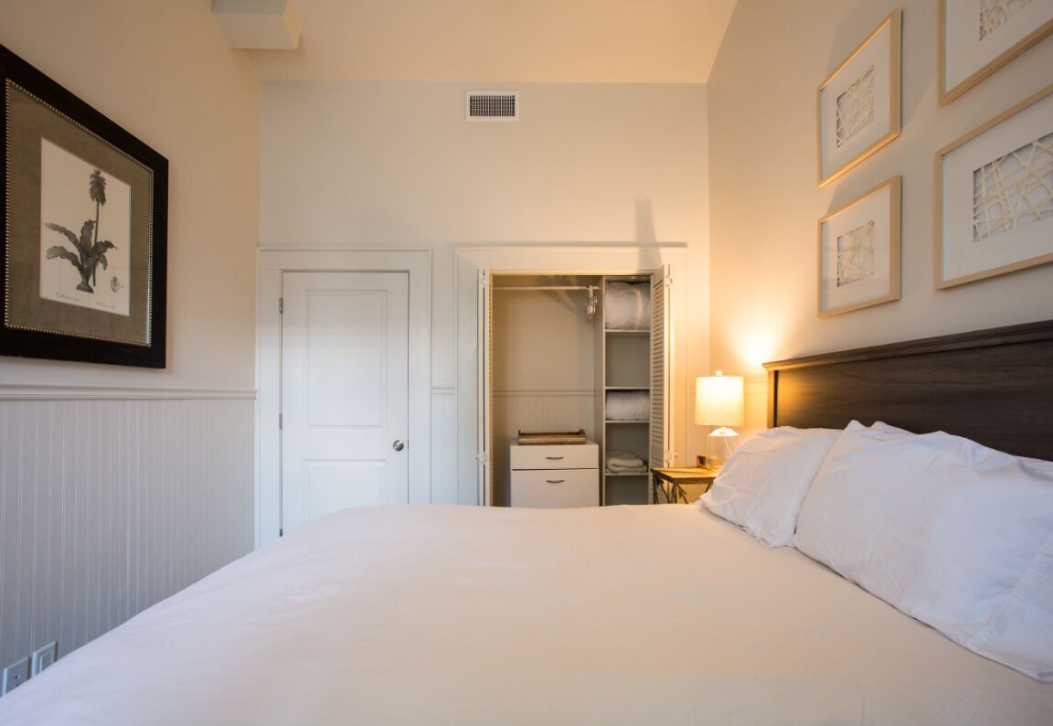 Une chambre d’hôtel comprenant un lit, une table de chevet avec une lampe, une armoire et une porte donnant sur une salle de bain.