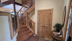 Una escalera de madera que sube a un piso superior, una puerta de madera y una pequeña mesa con una planta y un cuenco.